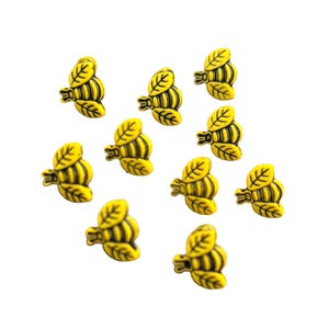 May include: A collection of yellow and black bee-shaped embellishments. Each bee has a yellow body with black stripes and leaf-shaped wings. These decorative elements are scattered against a white background.
