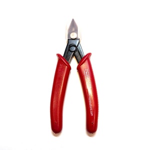 May include: Red handled wire cutters with a black body and a clear plastic tip protector. The tool has the text "Button Button" and "www.morebuttons.com" printed on one handle.