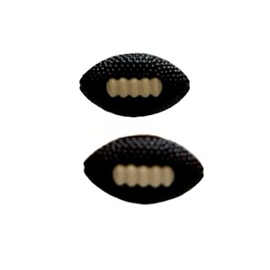 May include: Two black football-shaped objects with textured surfaces and tan-colored laces. The objects are positioned one above the other against a white background. The footballs appear to be miniature or decorative.