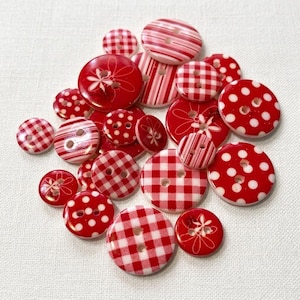 May include: A collection of round buttons in various sizes, featuring red and white patterns including polka dots, gingham checks, stripes, and floral line art designs. Each button has two or four holes for sewing, with a glossy finish throughout.