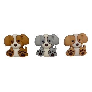 May include: Three decorative dog-shaped buttons. The buttons feature a sitting puppy design with brown, gray, and white color schemes. Each button has a white face, brown or gray ears, and brown paw prints.