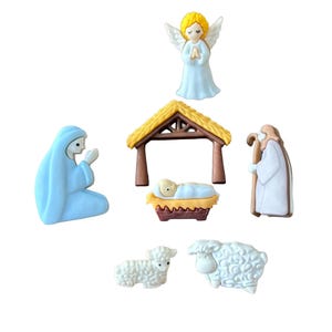 May include: A collection of miniature nativity scene figurines. The set includes a light blue Virgin Mary, a golden-haired angel, a stable, a shepherd, two white sheep, and the baby Jesus in a manger. The figurines are set against a white background.
