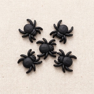 May include: Five small, matte black spider-shaped embellishments arranged in a cluster. Each spider features a rounded body and eight curved legs extending outward, crafted with a smooth, uniform finish and a consistent, detailed design.