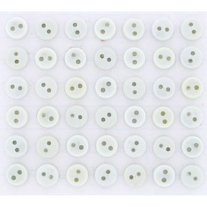 May include: A collection of small, round, off-white buttons with two holes each. The buttons are arranged in neat rows and columns, creating a grid-like pattern. The buttons are made of a smooth, possibly plastic, material.