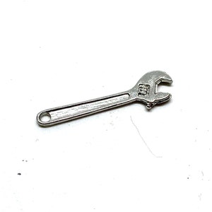 May include: A small, silver adjustable wrench, lying on a white surface. The wrench has a long handle with a hole at the end and an adjustable jaw at the other end. The wrench is a tool used for tightening or loosening nuts and bolts.