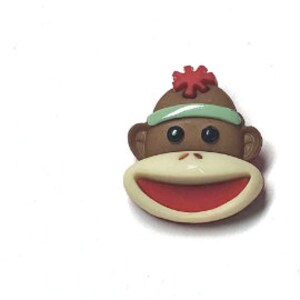 Puede incluir: Primer plano de un bot&oacute;n con la cara de un mono Paul Frank. El bot&oacute;n presenta una cabeza de mono marr&oacute;n con una diadema verde claro y una flor roja. El mono tiene una boca color crema con el interior rojo y ojos negros.
