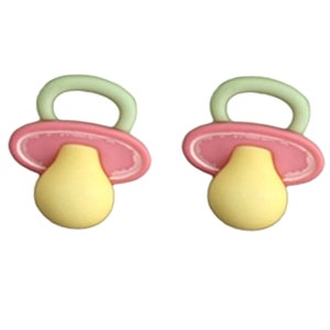 May include: Two pacifier-shaped charms. Each charm features a yellow nipple, a pink shield, and a green handle. The charms are designed with rounded edges and a smooth finish, suggesting a playful and soft aesthetic, suitable for baby-themed crafts.