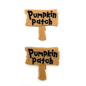 May include: Two small, tan-colored signs with the words "Pumpkin Patch" in black lettering. Each sign has a wooden post attached to the bottom. The signs are likely decorative items, possibly for fall or Halloween.