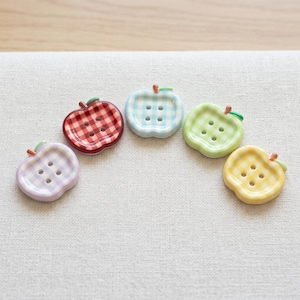 May include: Five apple-shaped buttons arranged in a semi-circle, each featuring a four-hole center and a gingham check pattern. The buttons are colored in purple, red, light blue, light green, and yellow, with a small brown stem on each top.