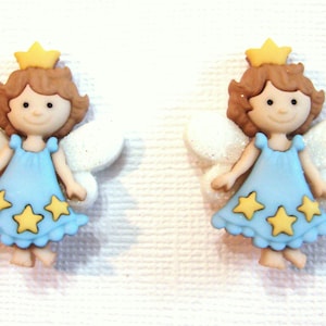 May include: Two decorative fairy figurines. Each fairy has brown hair, a yellow crown, and a light blue dress adorned with yellow stars. They have white, glittery wings and are smiling. The figurines are likely made of resin or a similar material.