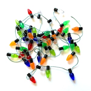 May include: A string of colorful Christmas lights with red, green, blue, orange, and clear bulbs. The bulbs are teardrop-shaped and attached to a green wire. The lights are scattered on a white surface.