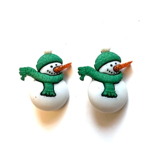 May include: Two snowman-shaped ornaments. Each snowman has a white body, a green hat and scarf, a carrot nose, and black dot eyes and mouth. The ornaments are on a white background.