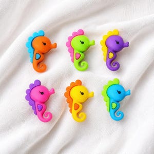 May include: Six seahorse-shaped buttons arranged in two rows. Each button features a distinct color combination: orange with blue, lime green with pink, purple with yellow, pink with purple, yellow with orange, and blue with green accents.