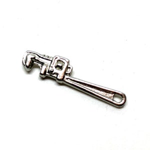 May include: A silver-colored adjustable wrench charm. The wrench is a miniature version of a real tool, with a handle and an adjustable jaw. The charm is made of a shiny metal and is set against a white background.