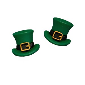 May include: Two green leprechaun hats with black bands and gold buckles. The hats are a vibrant green color and are set against a white background. The hats are a festive decoration.