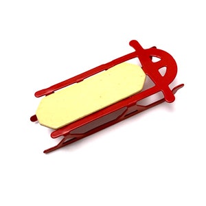 May include: A small, red metal sled with a light yellow seat. The sled has a classic design with curved runners and a simple, rectangular seat. The sled is designed for winter fun and outdoor activities.