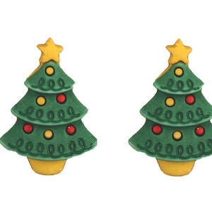 May include: Two Christmas tree-shaped ornaments. Each tree is green with red and yellow ornaments, a yellow star on top, and a yellow base. The ornaments have a whimsical, cartoon-like design.