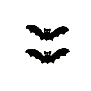 May include: Two black bat-shaped decorations with a white background. The bats have a simple design with pointed wings and small, white eye details. These Halloween-themed decorations are perfect for adding a spooky touch to any space.