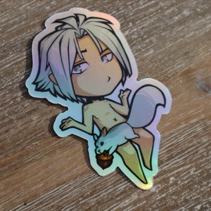 Puede incluir: Una pegatina holográfica con un personaje de dibujos animados con cabello blanco, torso desnudo y cola. El personaje sostiene una pequeña ardilla azul que sostiene una bellota.