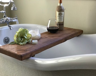 May include: A wooden bath tray with a glass of red wine, a candle, and a jar of bath salts. The tray is placed on the edge of a white bathtub.