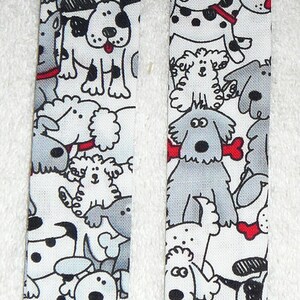 May include: Two fabric bookmarks with a white background and black and gray dog illustrations. One bookmark has a red button and the other has a black button.