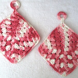 May include: Two crocheted pink and white pot holders with a loop for hanging. The pot holders are made with a textured stitch pattern.