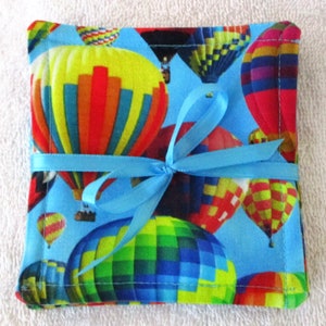 May include: Set of four blue fabric coasters with a hot air balloon print. The coasters are tied together with a blue ribbon.
