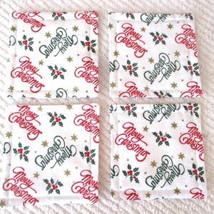Puede incluir: Conjunto de cuatro posavasos de tela blanca con un estampado navide&ntilde;o rojo y verde. El estampado presenta las palabras "Feliz Navidad" y "Felices Fiestas" con acebo y estrellas doradas.