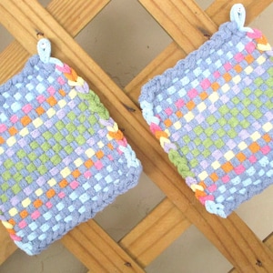 Puede incluir: Dos agarraderas de olla tejidas en azul y blanco con un patrón de cuadros en tonos de verde, naranja, rosa y amarillo.