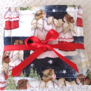 Puede incluir: Una peque&ntilde;a bolsa de regalo cuadrada de tela roja y blanca con una cinta roja atada alrededor. La bolsa est&aacute; decorada con una escena navide&ntilde;a de &aacute;ngeles cantando en la nieve.