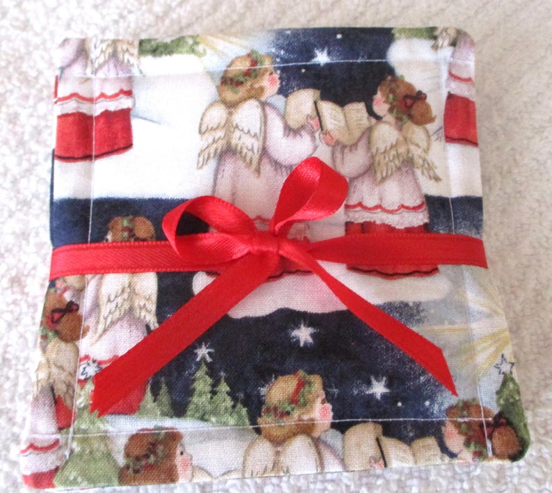 Puede incluir: Una peque&ntilde;a bolsa de regalo cuadrada de tela roja y blanca con una cinta roja atada alrededor. La bolsa est&aacute; decorada con una escena navide&ntilde;a de &aacute;ngeles cantando en la nieve.