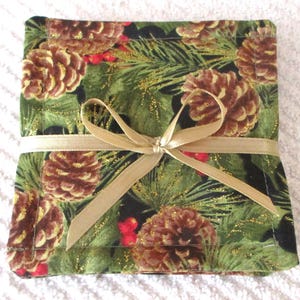 Puede incluir: Conjunto de cuatro posavasos de tela verde y negro con un patr&oacute;n de pi&ntilde;as y bayas de acebo. Los posavasos est&aacute;n atados con una cinta dorada.