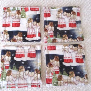 Puede incluir: Conjunto de cuatro posavasos cuadrados de tela con un dise&ntilde;o de &aacute;ngel navide&ntilde;o. Los posavasos son blancos con un fondo azul oscuro y presentan &aacute;ngeles cantando en un paisaje nevado. Los &aacute;ngeles llevan t&uacute;nicas blancas con detalles rojos y tienen halos dorados.