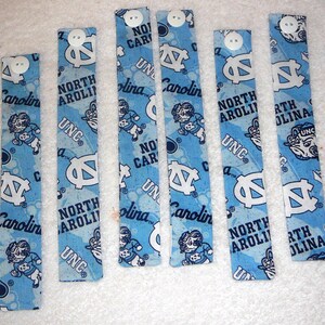 Peut inclure: Huit bracelets en tissu bleu et blanc avec le texte "North Carolina" et le logo UNC. Les bracelets ont des boutons blancs.