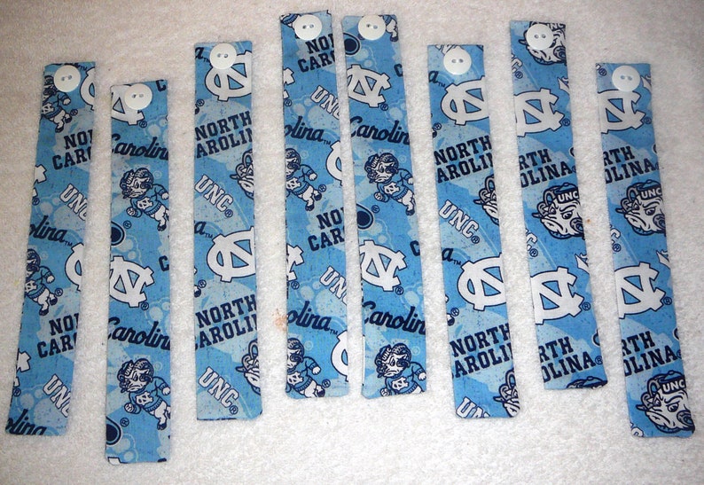 Peut inclure: Huit bracelets en tissu bleu et blanc avec le texte "North Carolina" et le logo UNC. Les bracelets ont des boutons blancs.