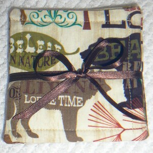 Puede incluir: Un posavasos de tela marr&oacute;n y beige con una cinta marr&oacute;n atada alrededor. El posavasos tiene un tema de naturaleza con las palabras "Believe in Nature" y "On Love Time" impresas en &eacute;l. El posavasos tambi&eacute;n presenta una silueta de oso marr&oacute;n.