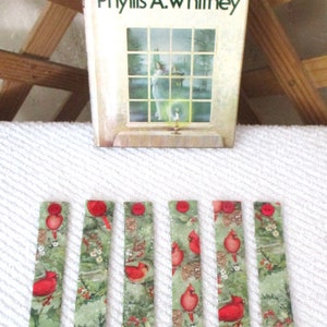 May include: Seven red and green Christmas-themed fabric bookmarks with a cardinal bird design. The bookmarks are approximately 10 inches long.