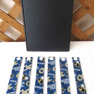 May include: Six blue and gold fabric bookmarks with the Georgia Tech logo and a yellow bumblebee design. The bookmarks have a white button at the top.