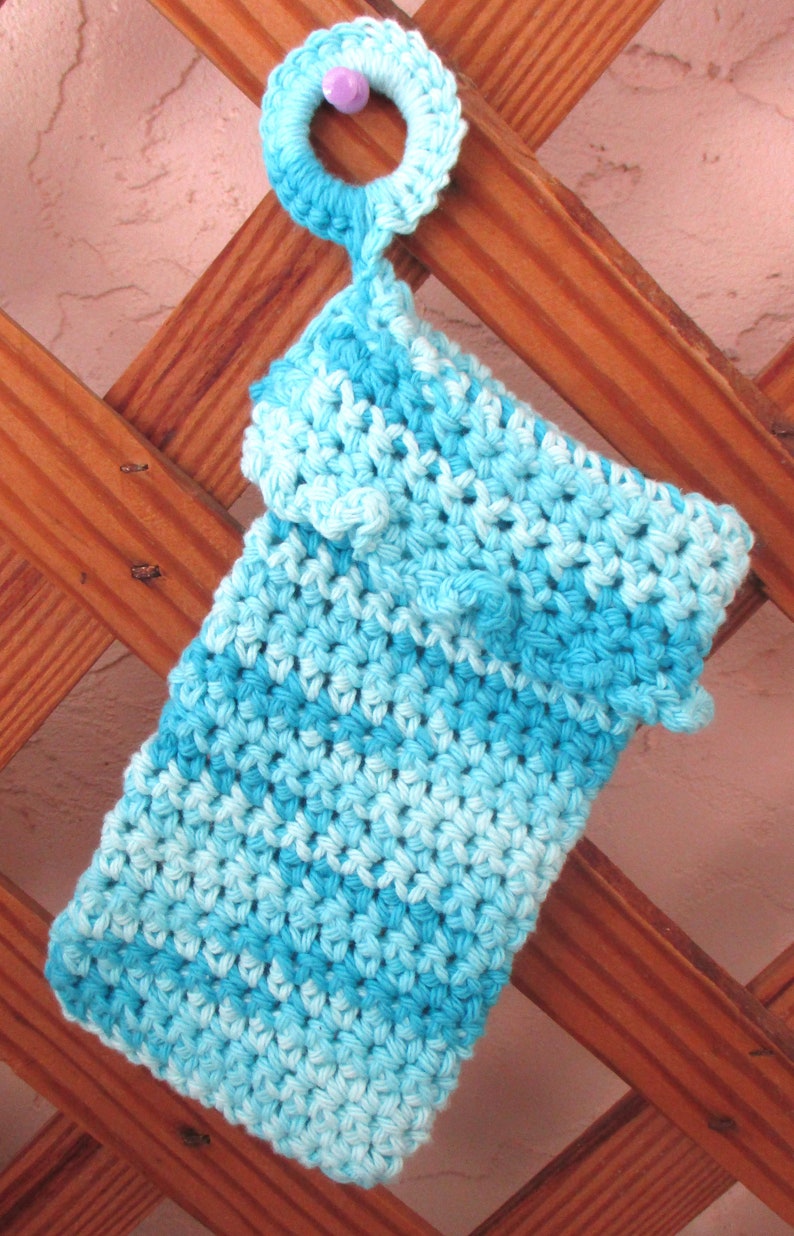 May include: A blue and white crocheted dishcloth with a crocheted loop at the top. The dishcloth is hanging on a wooden trellis.