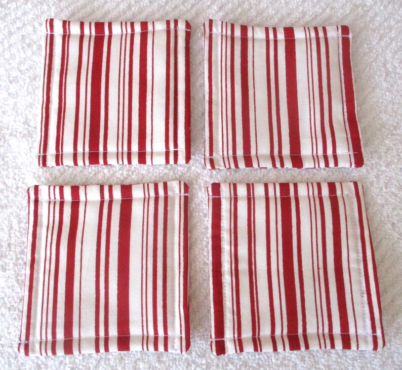 Puede incluir: Conjunto de cuatro posavasos de tela a rayas rojas y blancas. Los posavasos son cuadrados y tienen un dise&ntilde;o acolchado.