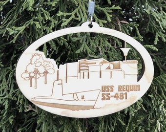 May include: A wooden oval ornament with a laser-cut design of a submarine and the text "USS Requin SS-481".