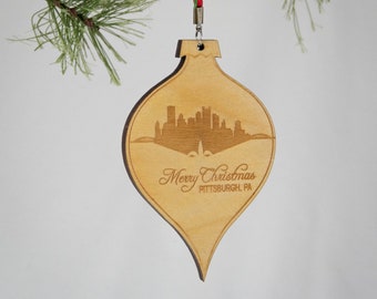 May include: Wooden Christmas ornament shaped like a teardrop with a laser-engraved silhouette of the Pittsburgh skyline and the text "Merry Christmas Pittsburgh, PA".