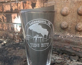 May include: A clear glass pint glass with an etched design of a cityscape with the text "McKeesport, PA" and "Tube City".