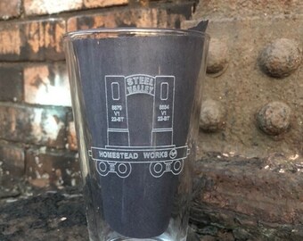 May include: A clear glass pint glass with a black and white design of a train car with the text "STEEL VALLEY" and "HOMESTEAD WORKS".