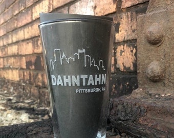 May include: A black glass pint glass with a white silhouette of the Pittsburgh skyline and the text "Dahntahn Pittsburgh, PA".