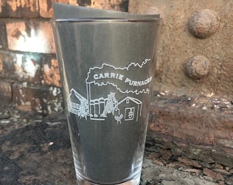 May include: A clear glass pint glass with an etched design of a factory with the text "Carrie Furnaces" above it.
