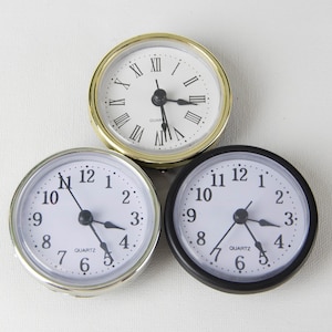 May include: Three round analog clocks with white faces and black hands. The clock on the left has a silver rim, the clock in the middle has a gold rim, and the clock on the right has a black rim.