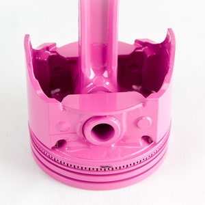 Op de afbeelding: Een roze metalen zuiger met een drijfstang. De zuiger is een gebruikelijk onderdeel van een verbrandingsmotor.