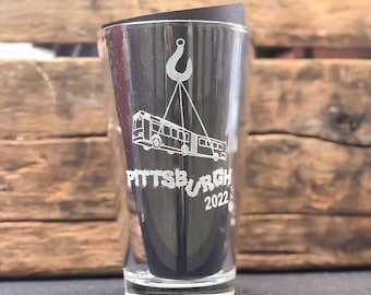 May include: A clear glass shot glass with a design etched into the side. The design features a bus being lifted by a hook with the text "PITTSBURGH 2022" underneath.