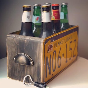 May include: A wooden six-pack beer carrier with a Pennsylvania license plate design. The license plate reads "PENNSYLVANIA NO.6.152". The carrier is filled with six bottles of beer.